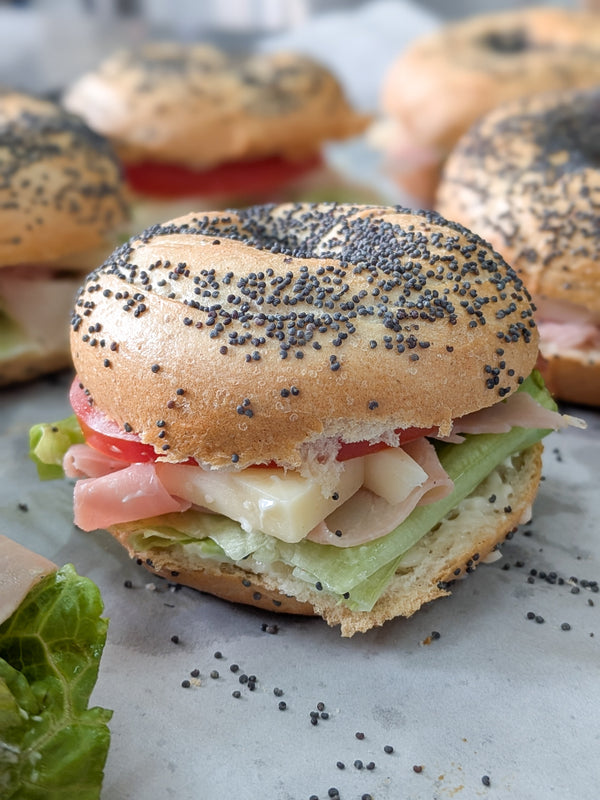 Bagel sandwich with ham, cheese, and lettuce on a marble surface
