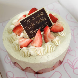 A strawberry cake with two layers, buttery cake with vanilla cream and fresh strawberries, with a decorative topper that reads 'To a real tough cookie, Happy Birthday!' on a pink floral background.